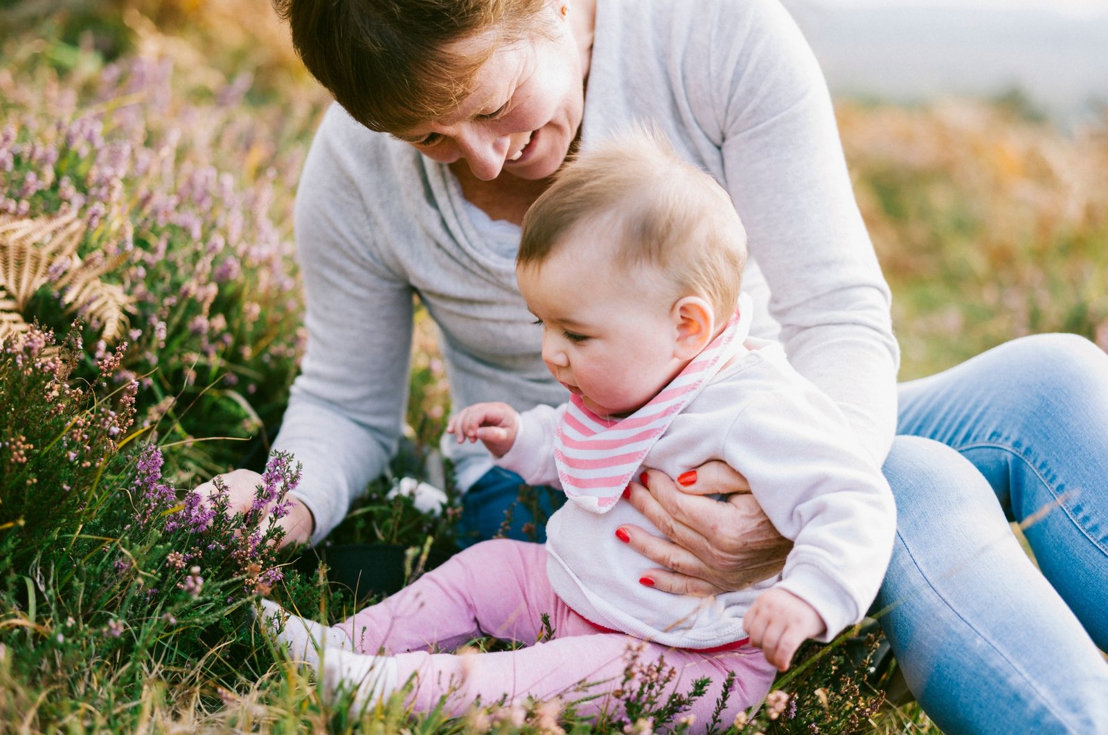 A woman sitting on the ground holding a young baby girl.